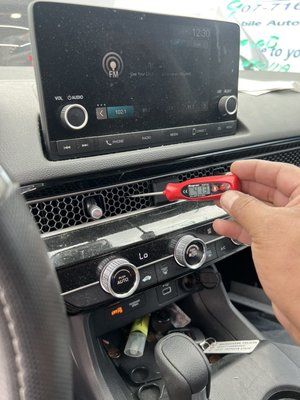 A person is holding a screwdriver in front of a car dashboard.