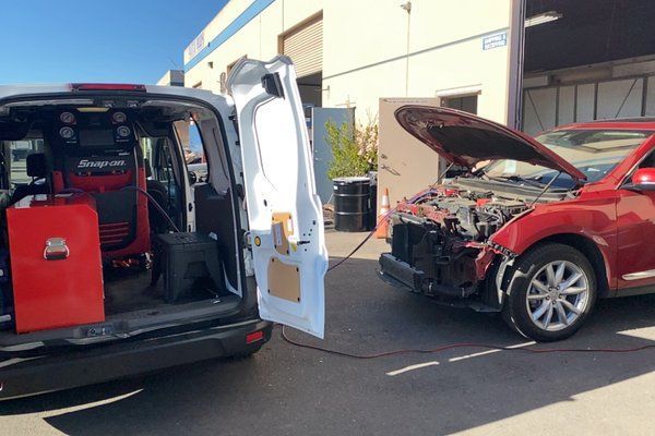 A red car is parked next to a white van with the hood open.