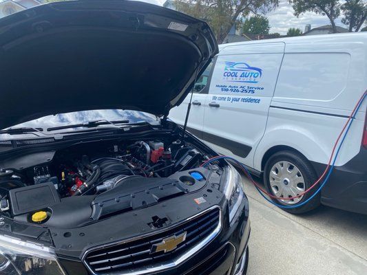 A black car with the hood up is being serviced by a white van.