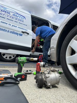A man is working on a car compressor next to a van.