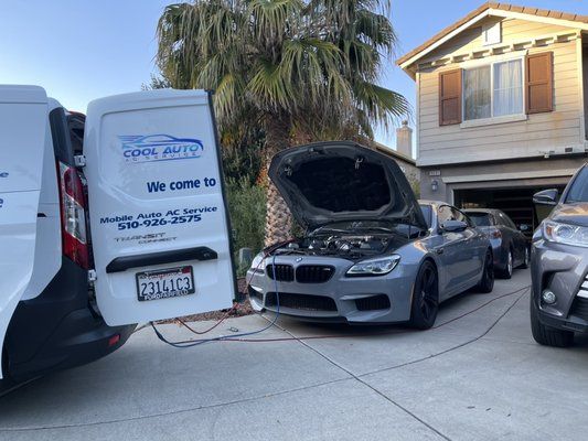 A bmw is being serviced in a driveway next to a van.