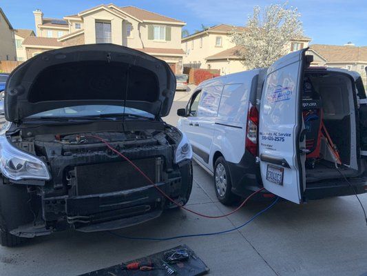 A car with the hood up is being serviced by a van.