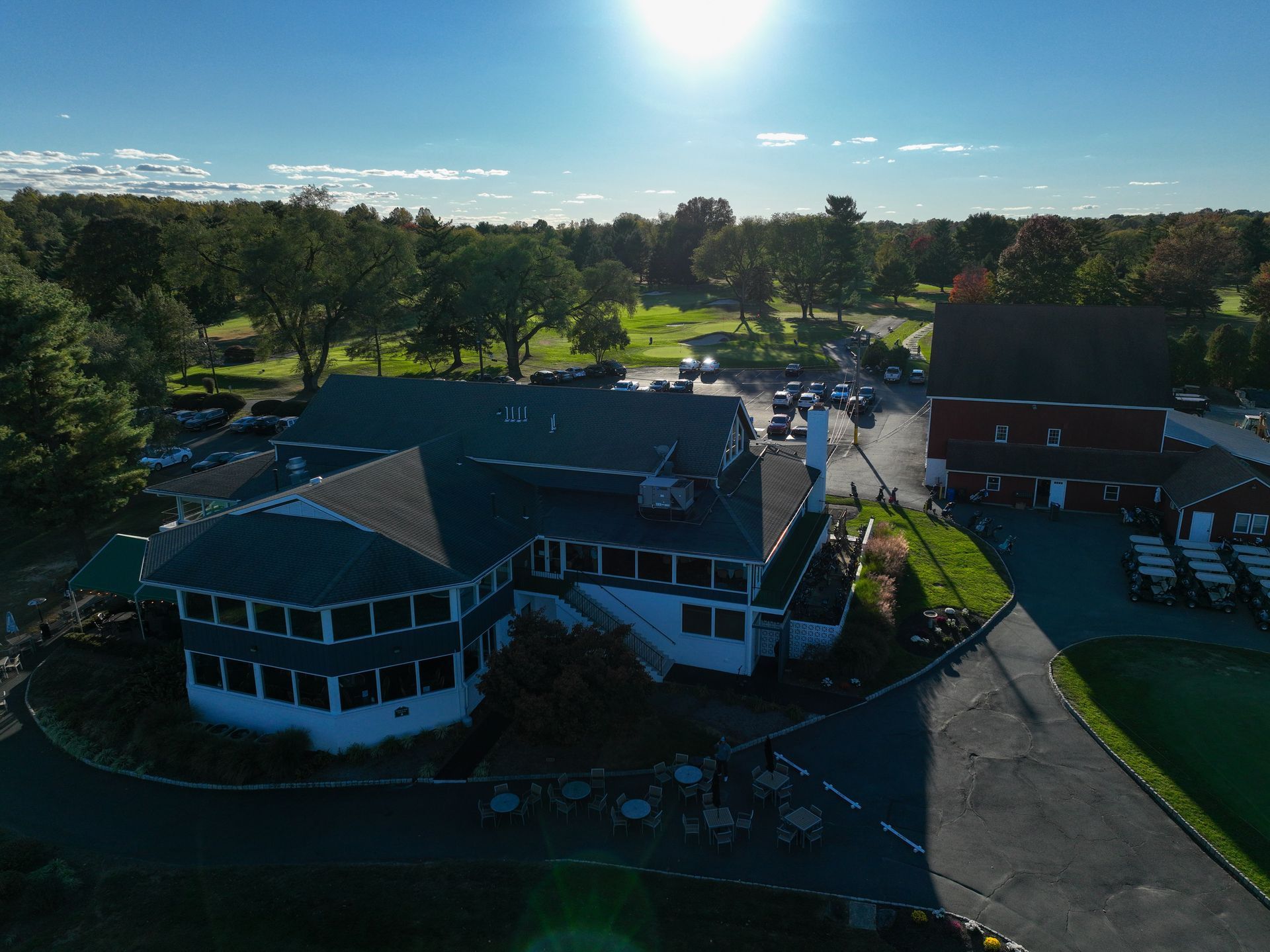 Aerial view of a golf club building with a driveway, adjacent to a green space with trees and golf carts for membership