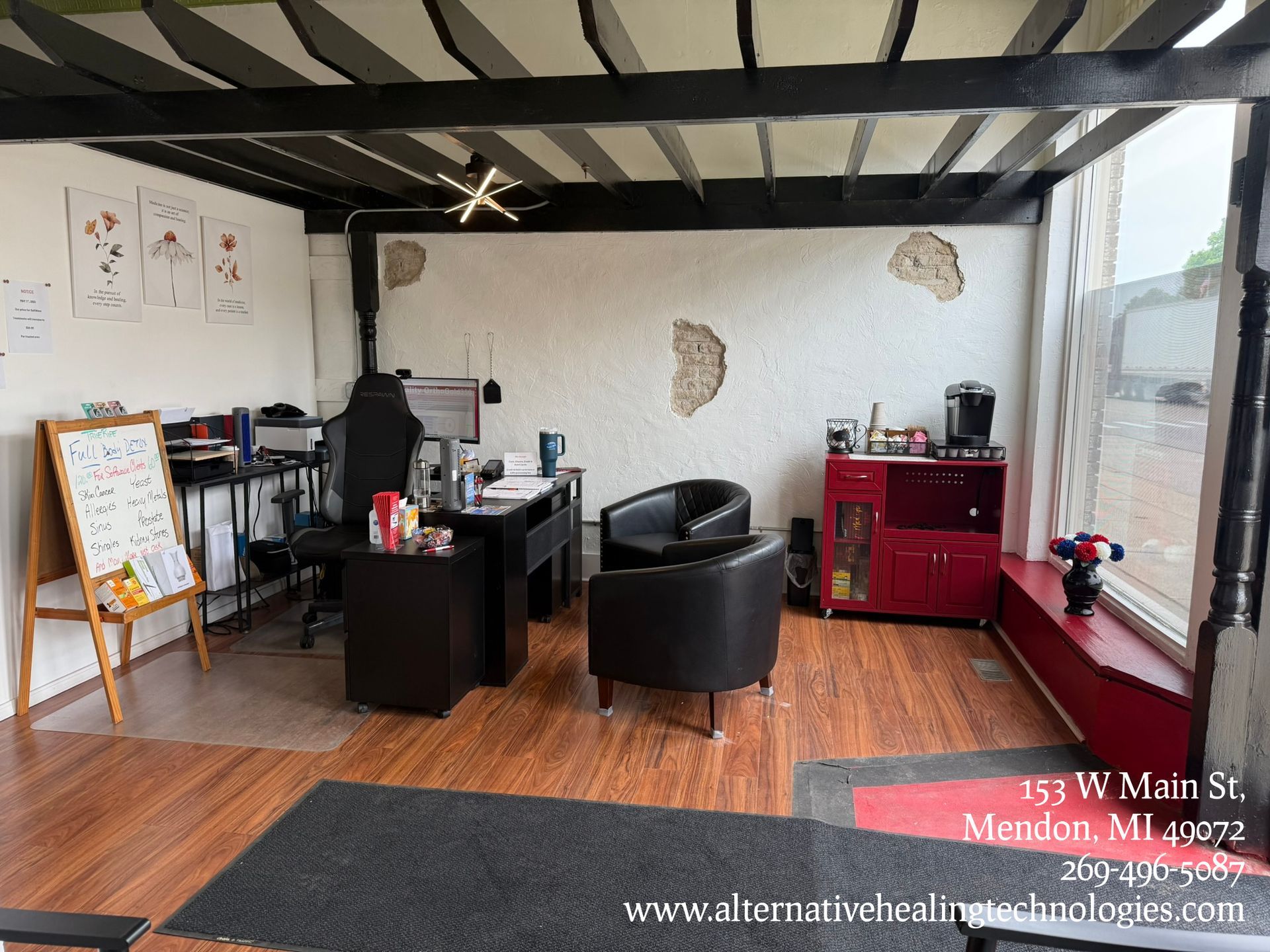 Office interior with desk, chairs, and coffee station; window to the right, wood and gray tones.