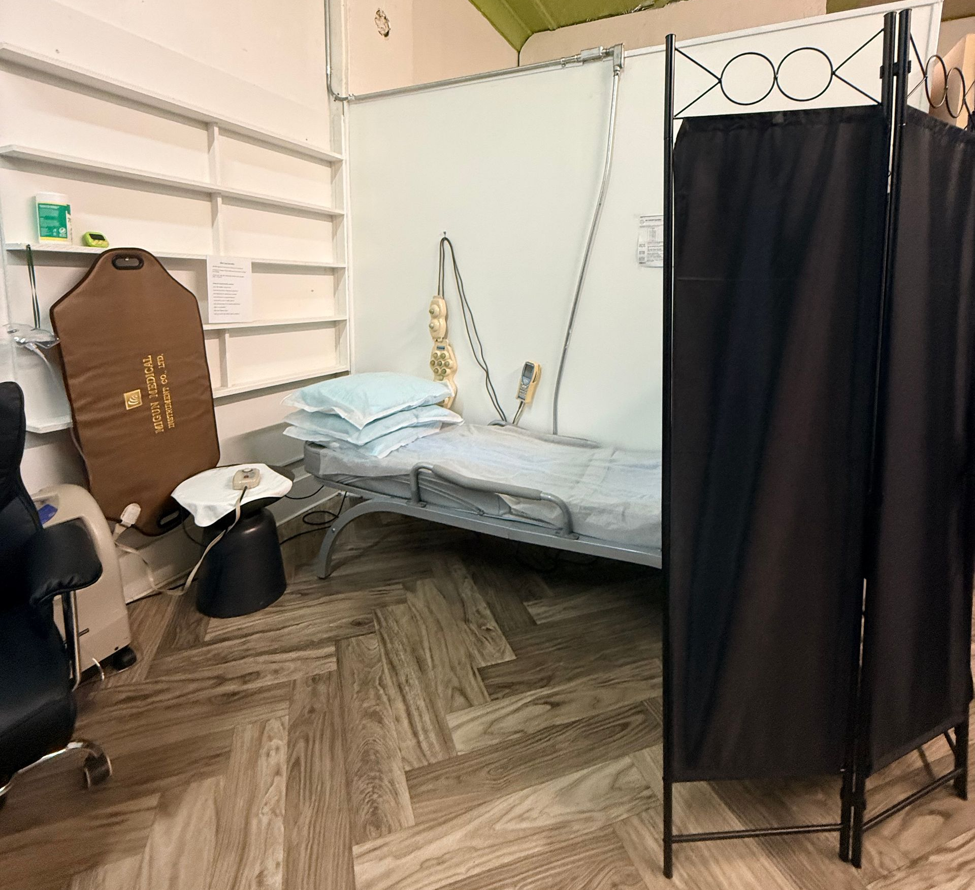Small room with a Med Bed, shelves, chair, and a black privacy curtain on a herringbone floor.