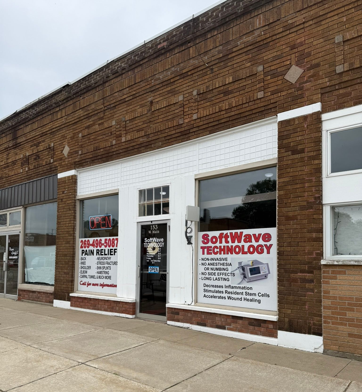 Brick storefront with white doors and windows, featuring tech service posters and signs on a sidewalk.