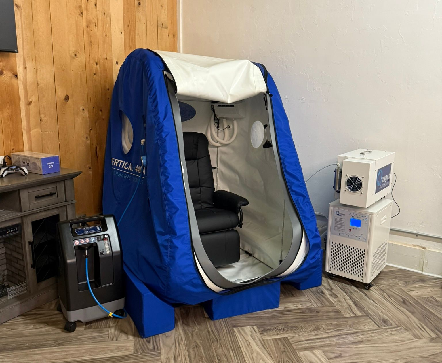 Blue treatment booth with white interior in a wood-paneled room, beside a small medical device cabinet.
