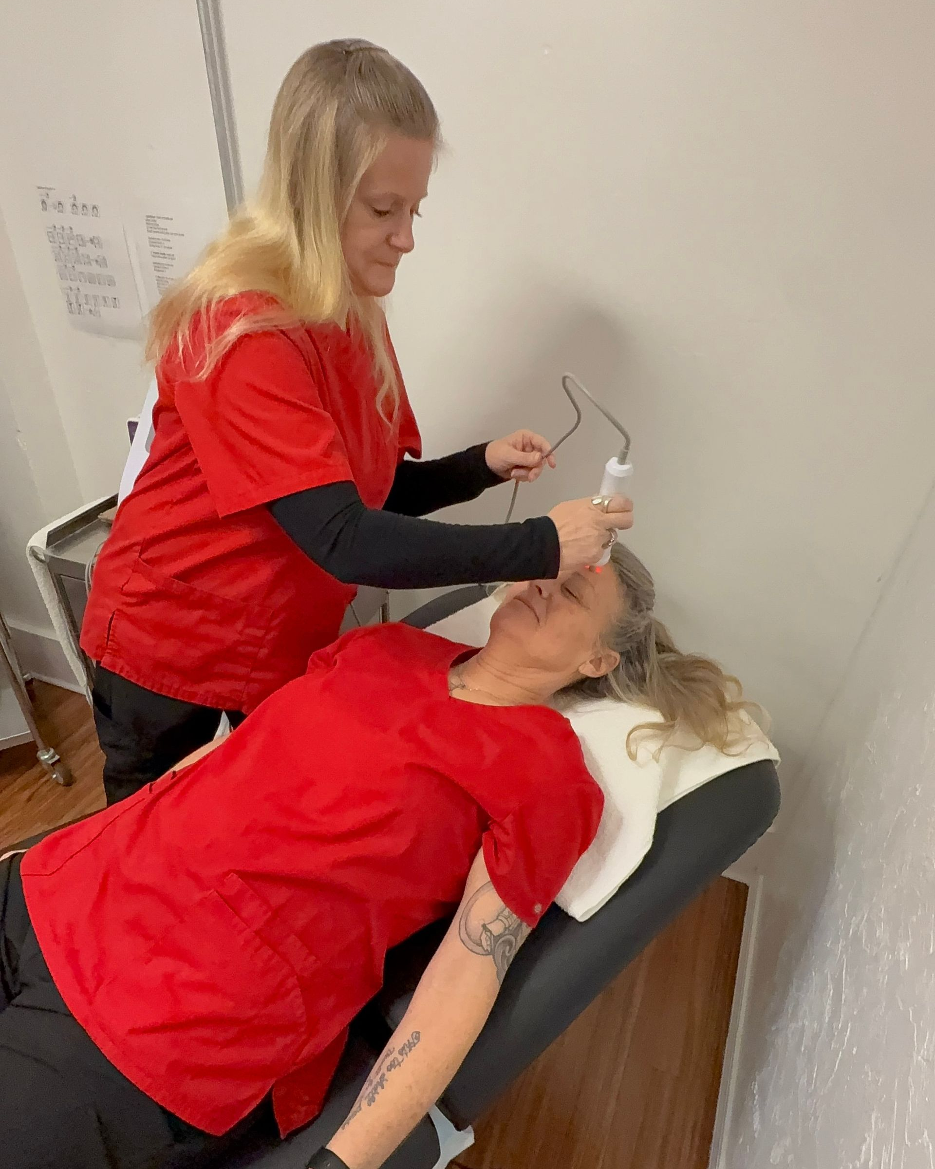 Two women in red tops using the body sculpting machine to tighten loose skin on the face.