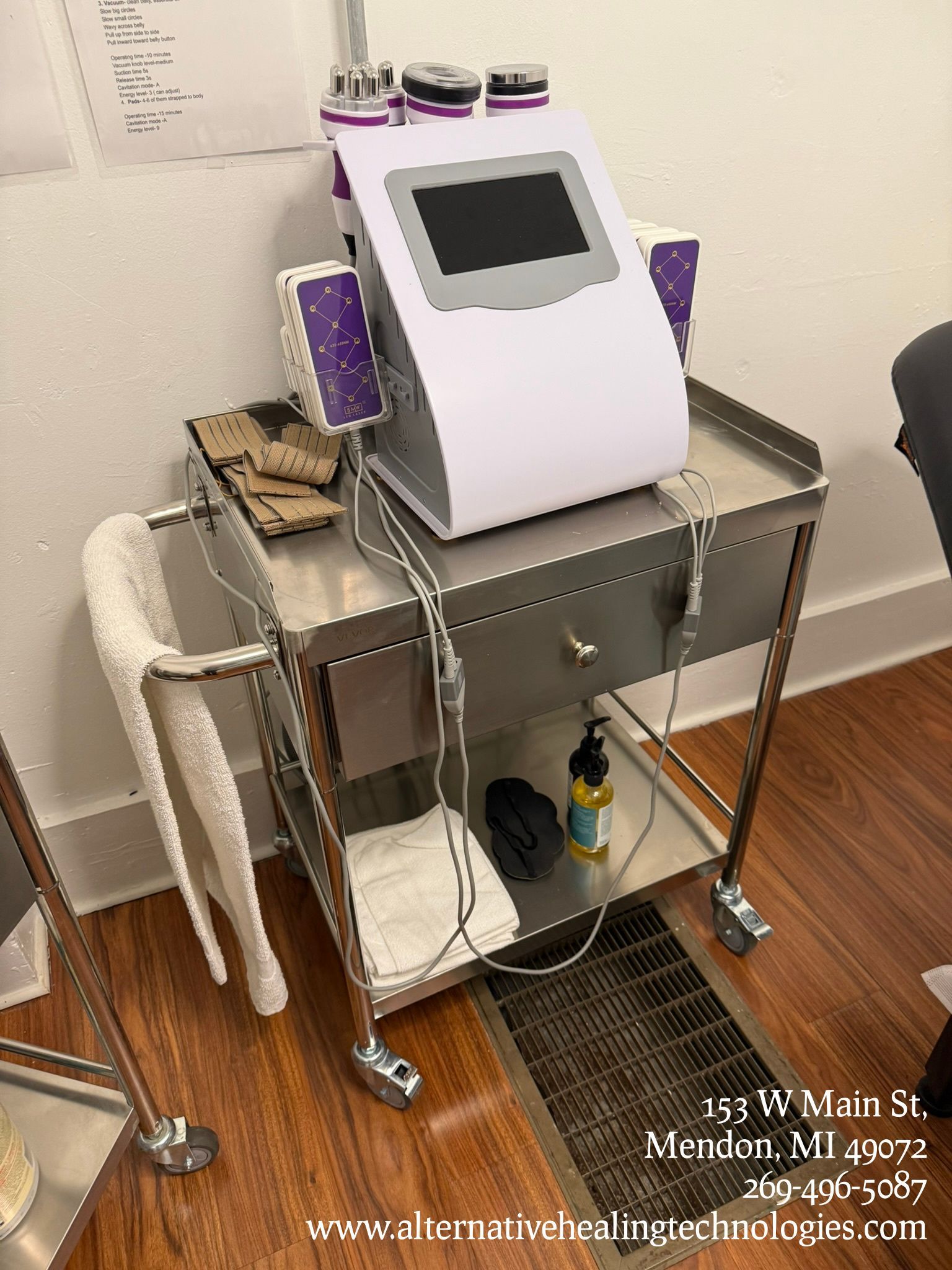 A white aesthetic machine with a screen sits on a metal cart with towels and supplies in a clinical treatment room.