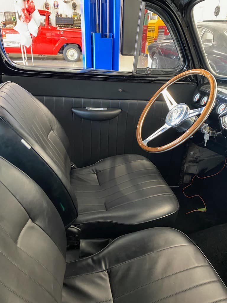 Vintage car interior with black seats and wood-rim steering wheel in a garage