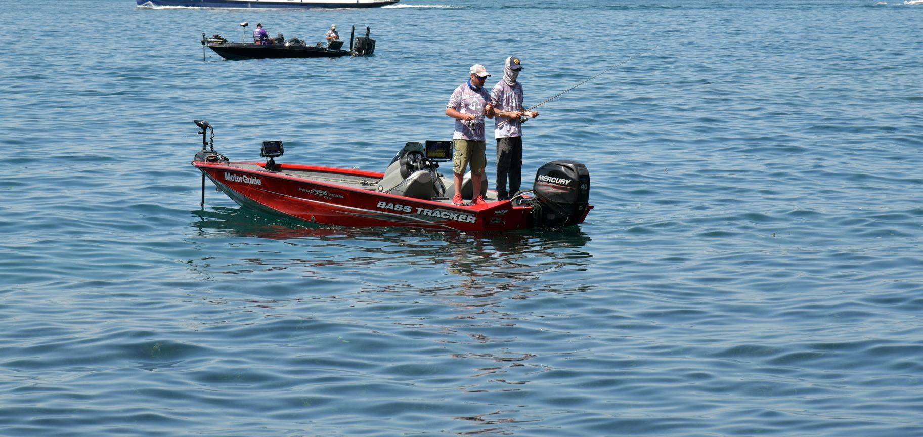 Two men are fishing in a red boat on a lake.