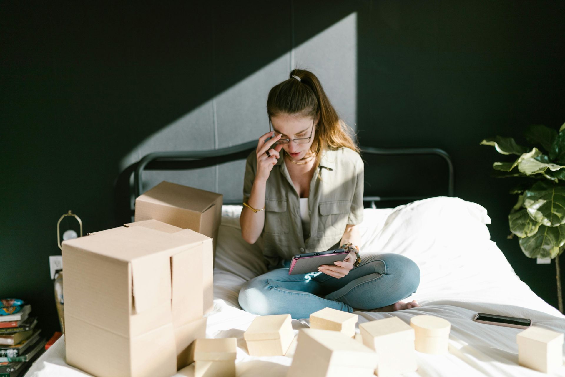 A woman is sitting on a bed with boxes and talking on a cell phone.