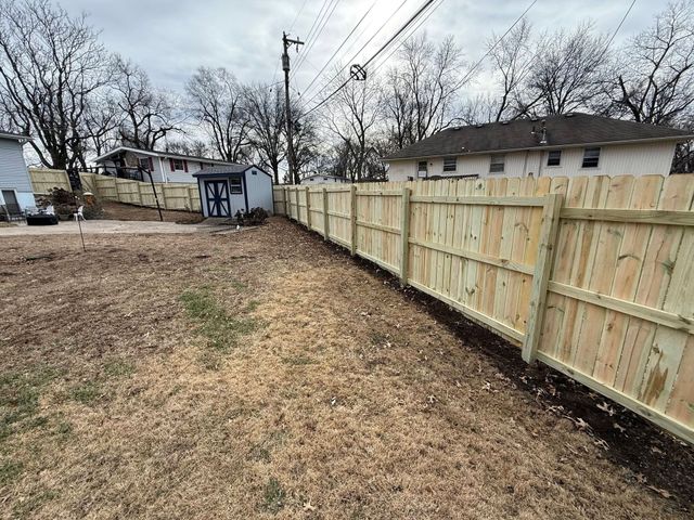 Backyard with a new wooden fence along the right side and a bare yard under cloudy sky