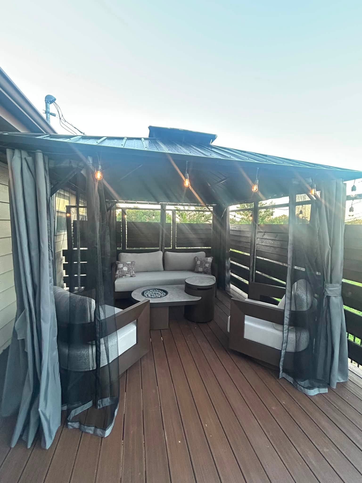 Covered outdoor deck with lounge seating, curtains, and a woven roof in bright daylight