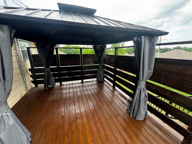 Covered wooden deck with gray curtains, black railings, and wet floor overlooking greenery