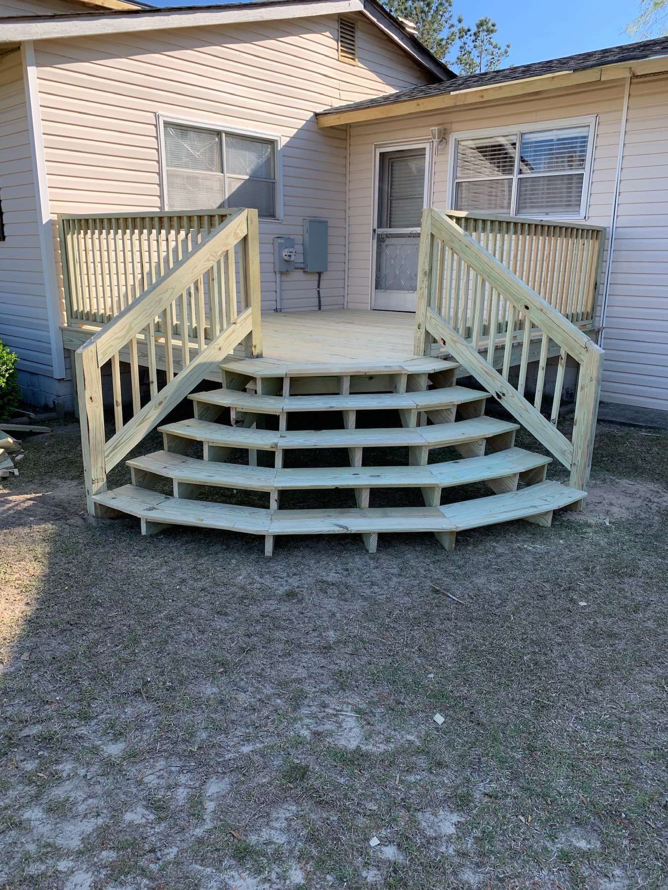 Front porch with wide curved wooden steps and railings on a beige house.