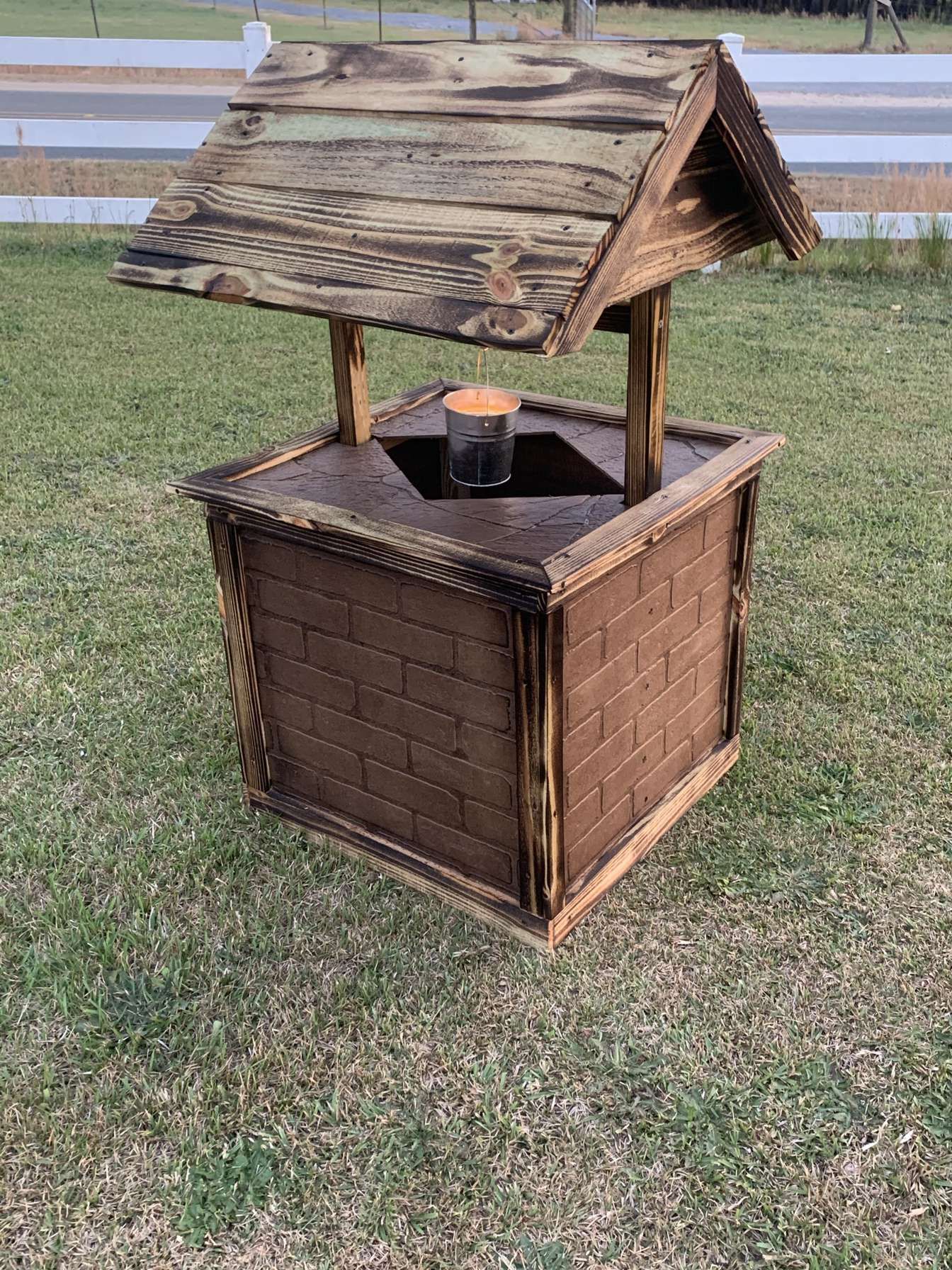Weathered wooden bird feeder with a pitched roof on a grassy lawn near water