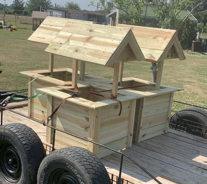 Wooden cart with a small roofed structure on a trailer, parked outdoors on grass.