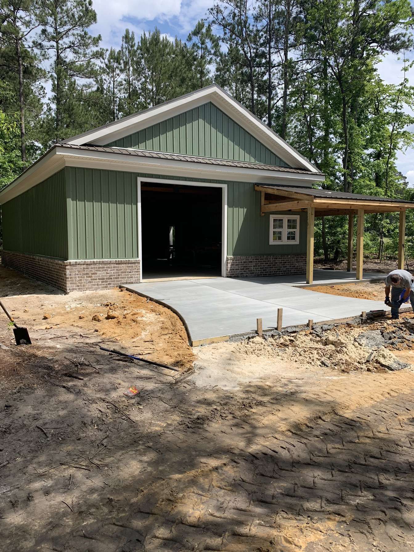 Green barn-style garage under construction with a concrete driveway and small covered porch.