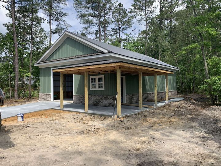 Small green house under construction with a front porch in a wooded area