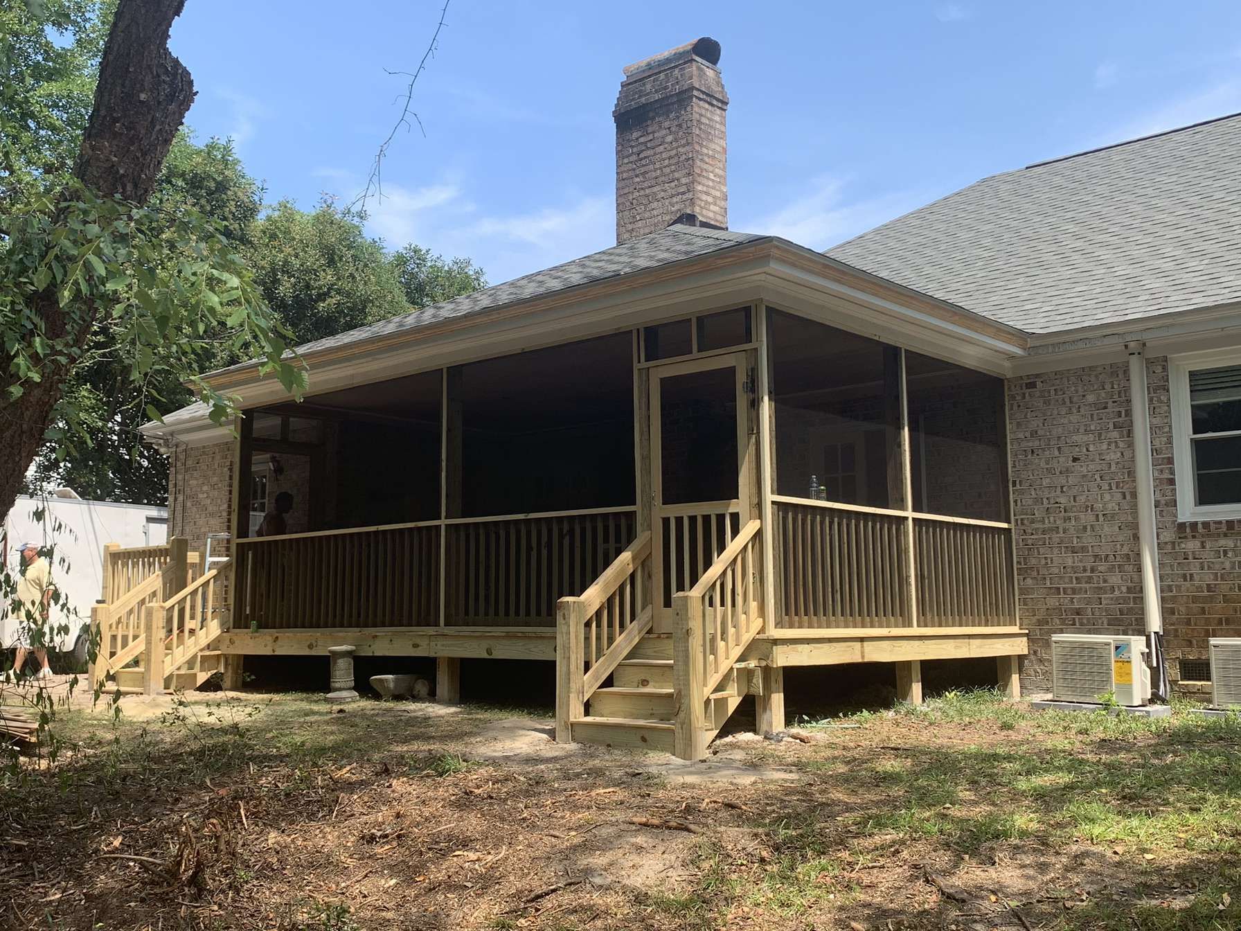 House with a covered wooden porch, steps, and brick chimney on a grassy yard