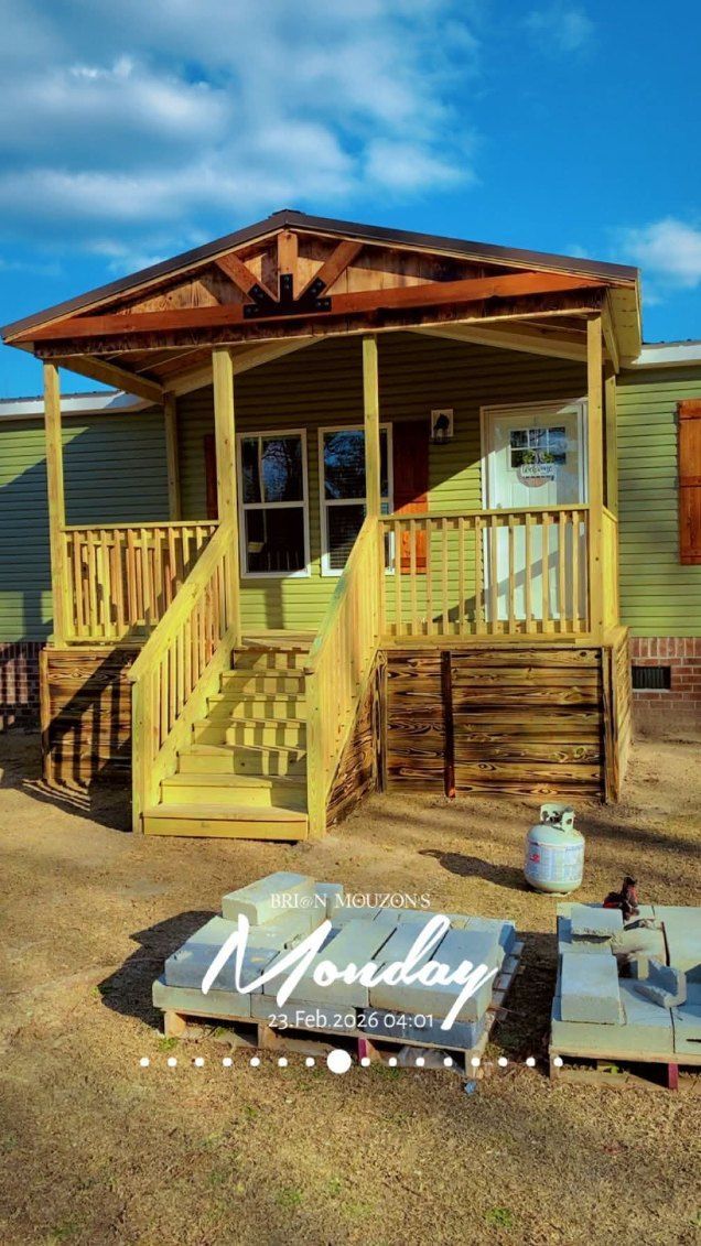 Yellow cabin porch with stairs, wooden railings, and a small sign in the yard under a blue sky