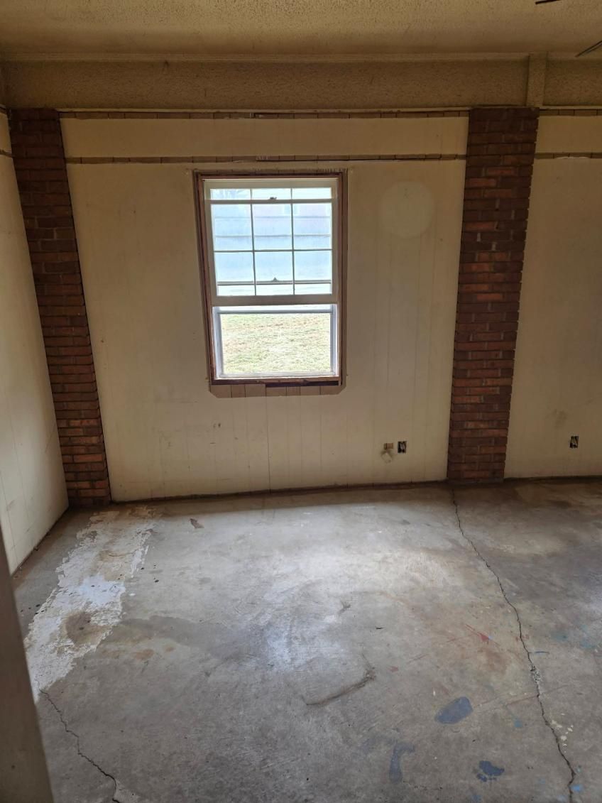 Empty room with unfinished concrete floor, small window, and exposed brick columns.