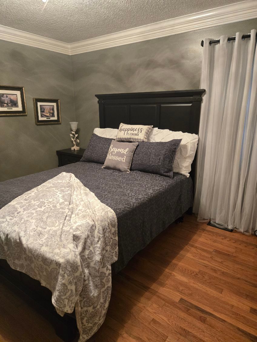 Cozy bedroom with dark wood bed, gray walls, patterned bedding, framed art, and hardwood floors.