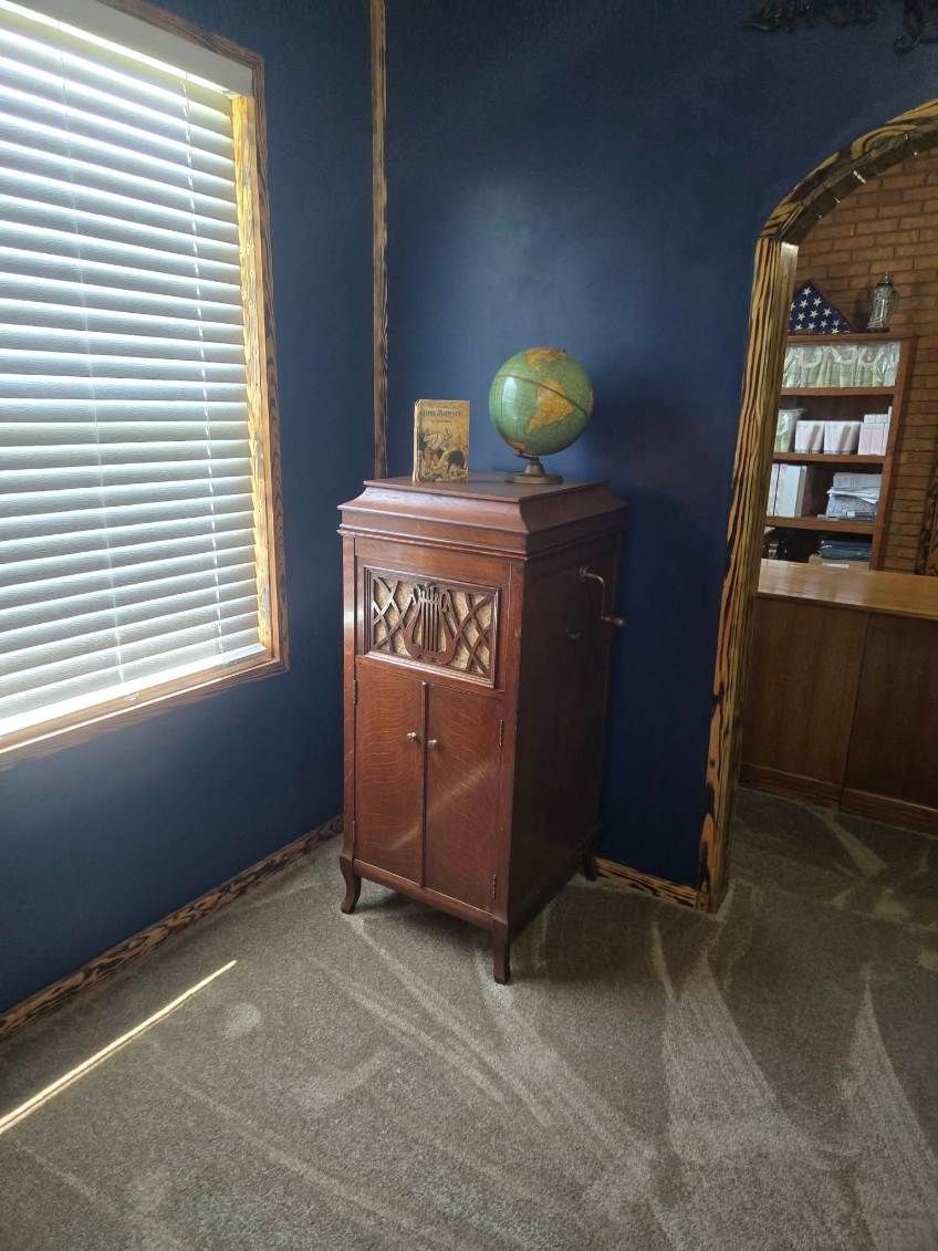 Blue room with window blinds, carved wooden cabinet, globe, and arched doorway.