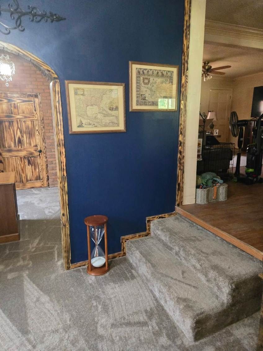 Blue wall with framed art beside a carpeted stair step and doorway into a home interior.