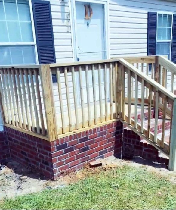 Wooden porch railing and steps on a brick-faced house entrance with white door and blue shutters