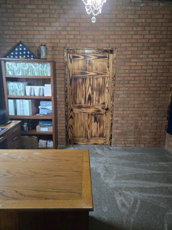 Brick room with wooden door, bookshelf, chandelier, and table in the foreground.