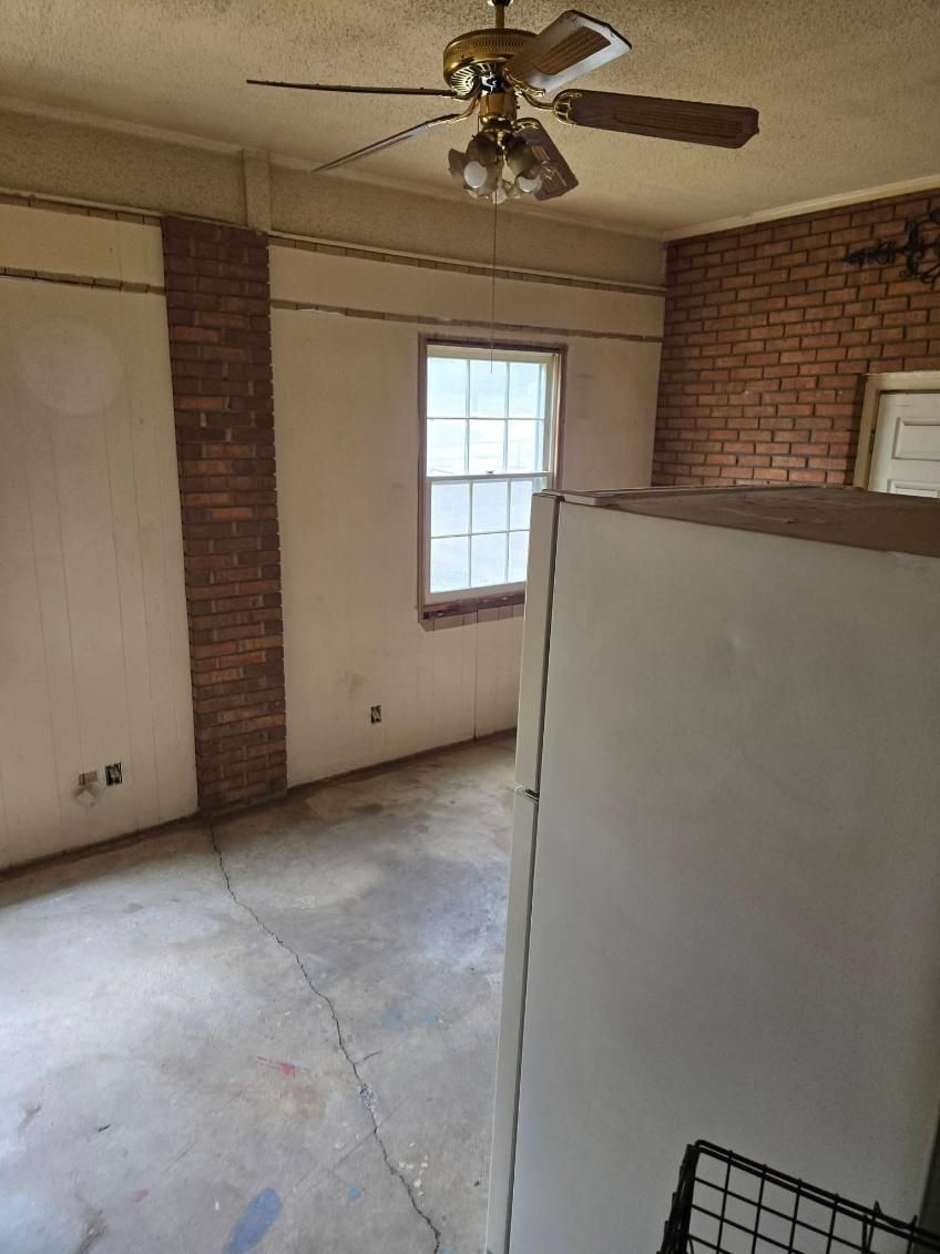 Empty room with brick walls, a window, ceiling fan, and a white cabinet in the foreground