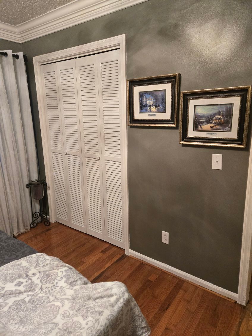 Bedroom corner with white closet doors, two framed pictures, gray walls, and hardwood floor