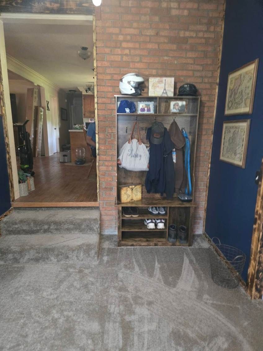 Indoor entryway with brick wall, coat rack shelf, mirror, and framed pictures on a blue wall.
