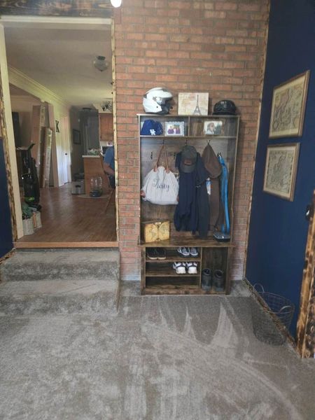 Indoor entryway with brick wall, coat rack, and blue accent wall leading to a hallway