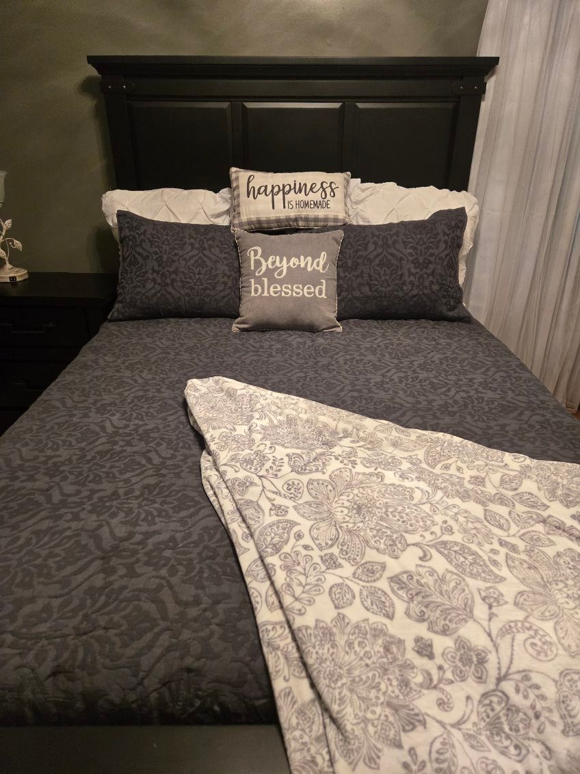 Neatly made dark gray bed with pillows and a patterned throw in a bedroom