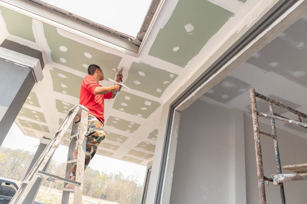 A Construction Worker Wearing Gloves Uses A Trowel To Plaster The Wall — HJK Plastering In South Lismore, NSW