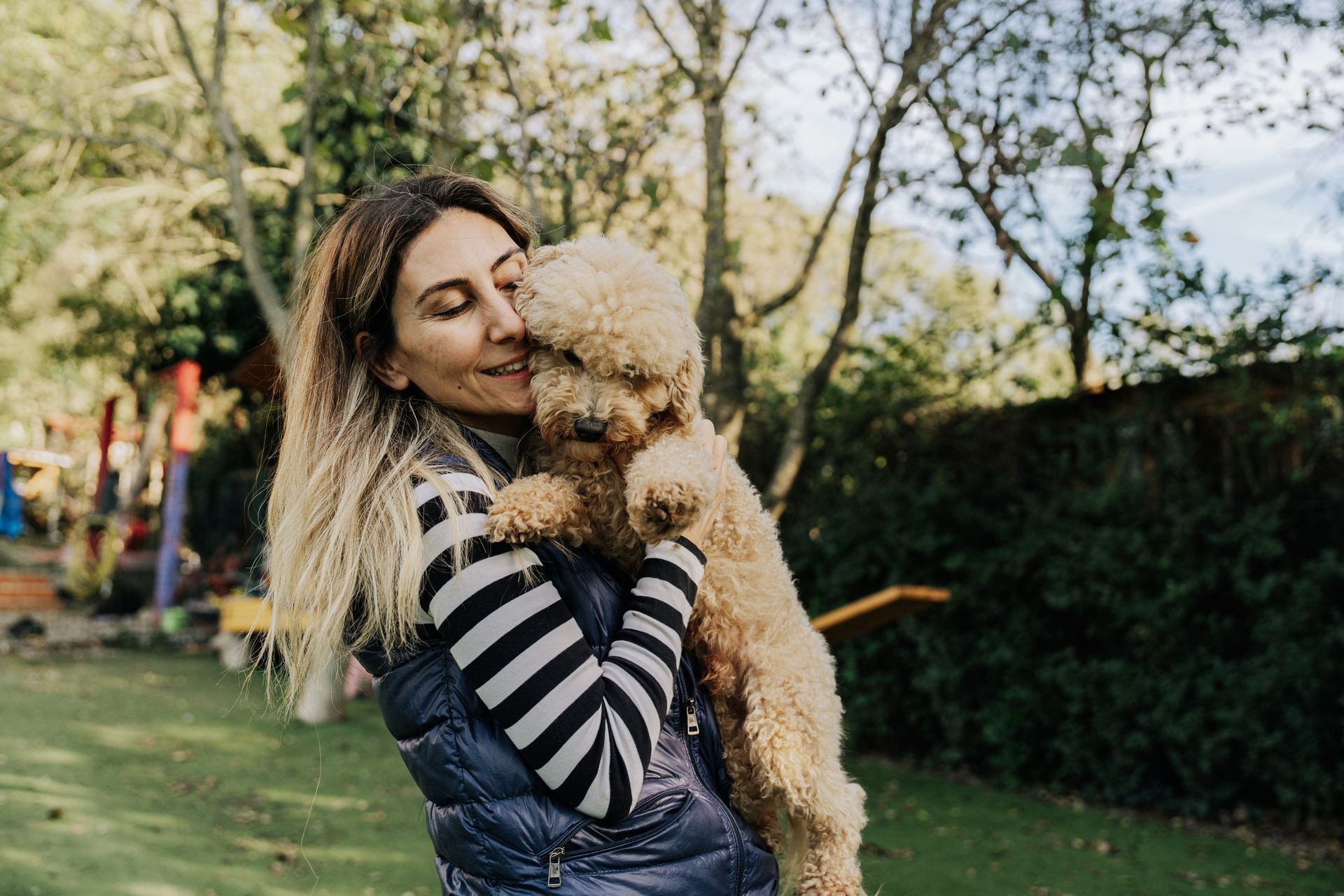 Woman in a striped sweater holding a fluffy dog in a sunny park