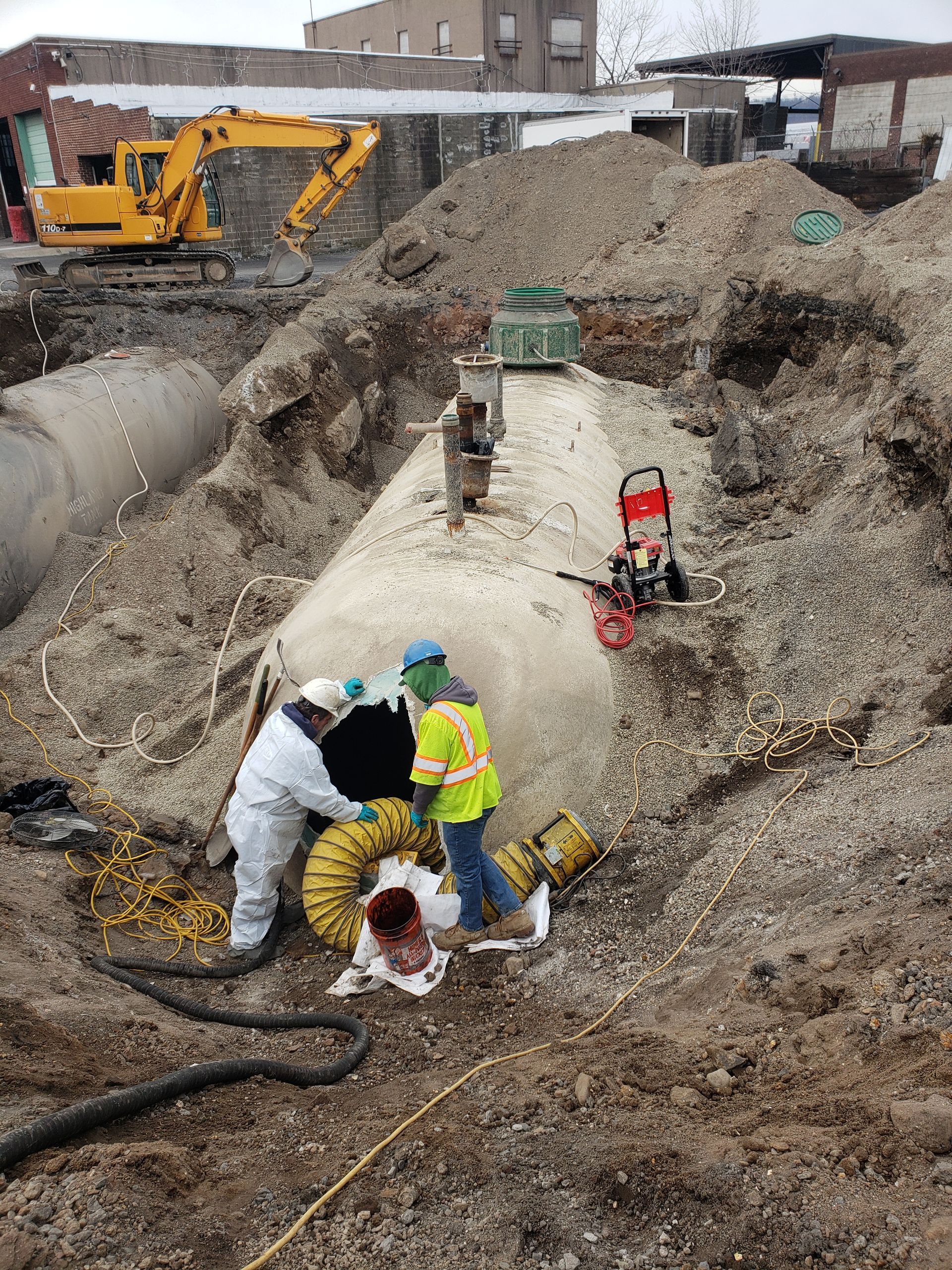 Workers in protective gear excavating a large underground tank in a construction site.