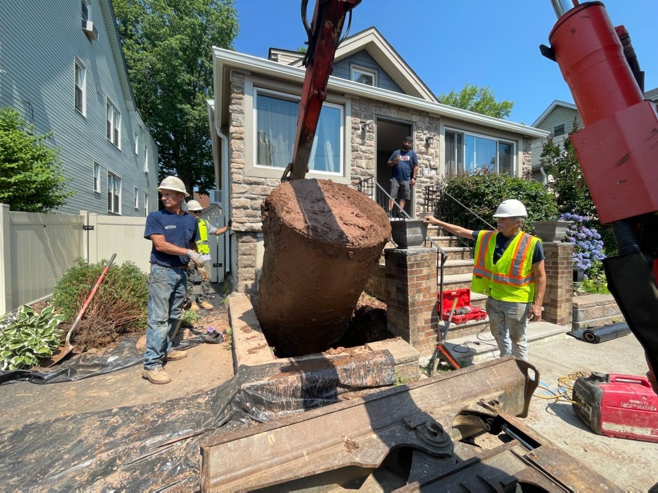 Workers remove a large, rusty object from a hole next to a stone house. Sunny day.