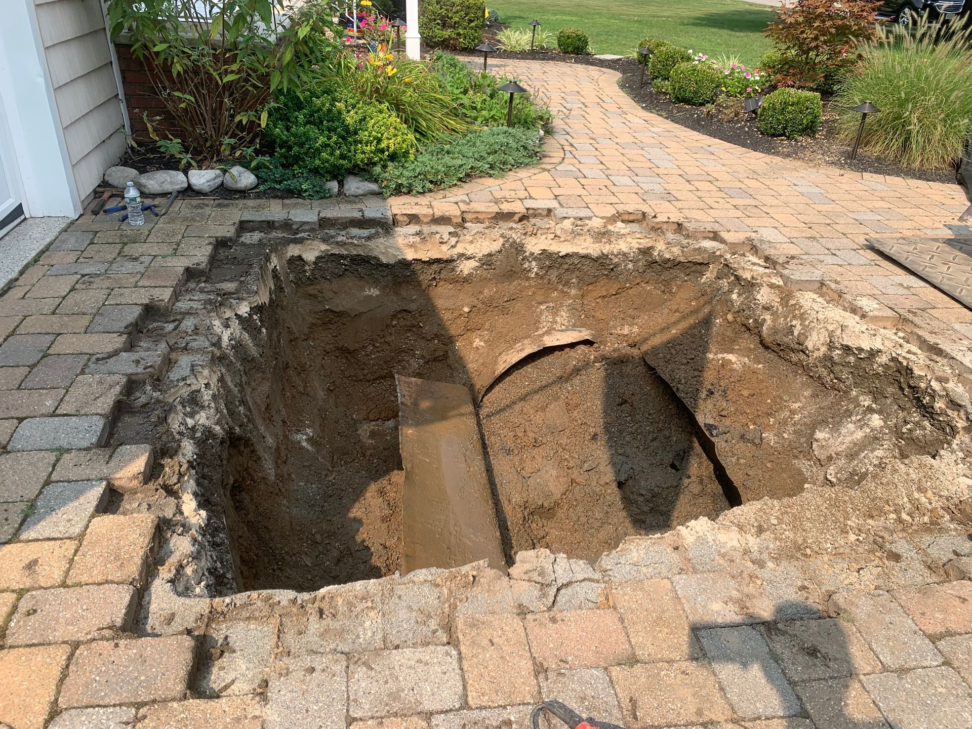 Large hole dug into a brick patio near a house. Earth and brick debris surround the pit.