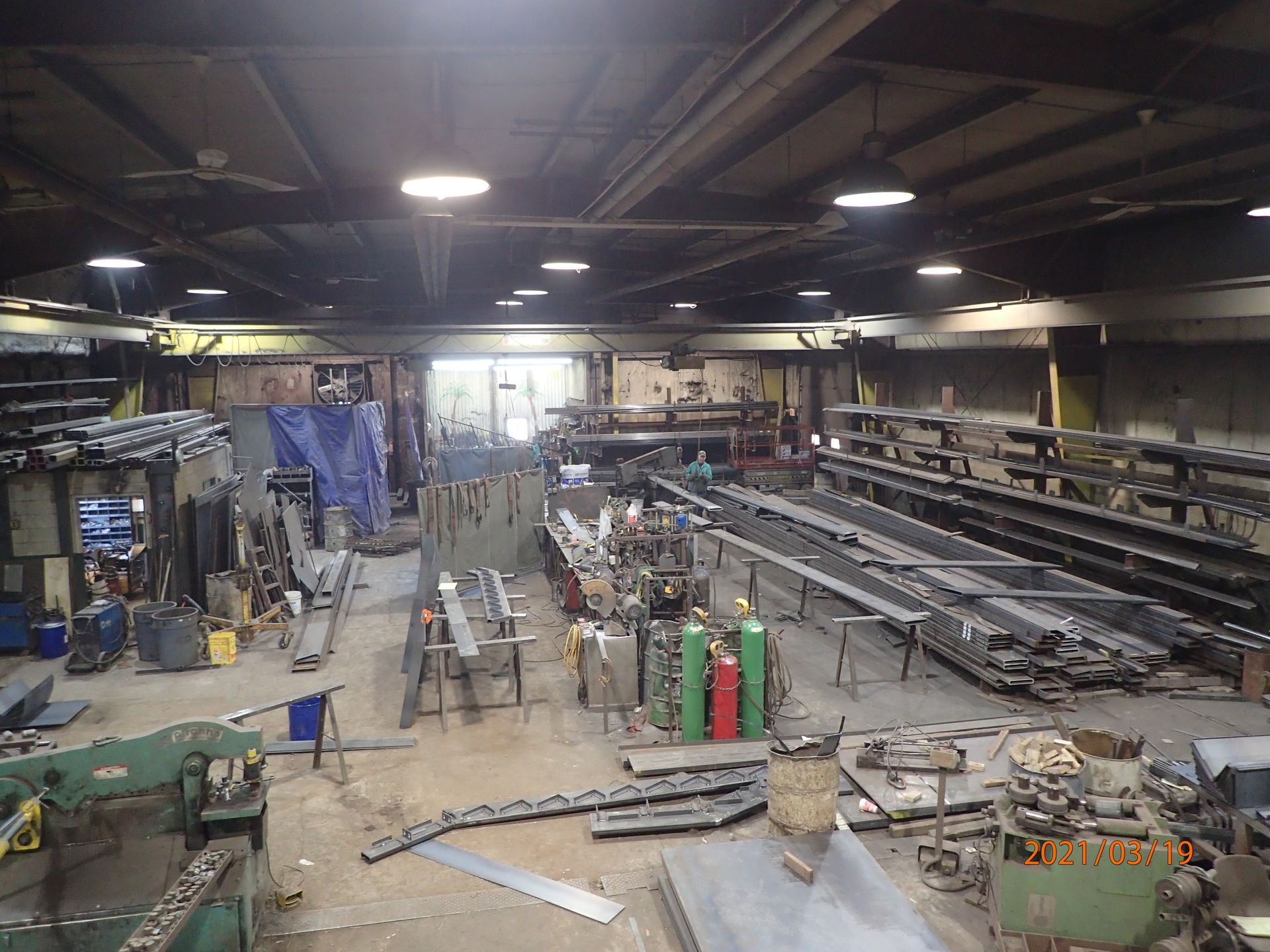 Interior view of a cluttered metal workshop with welding tanks and metal parts.