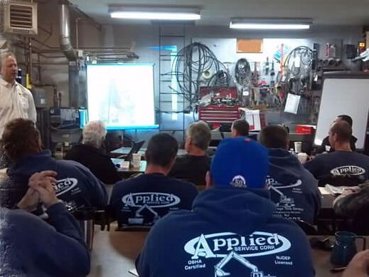 A presentation in a workshop setting. Men in blue shirts with the company name