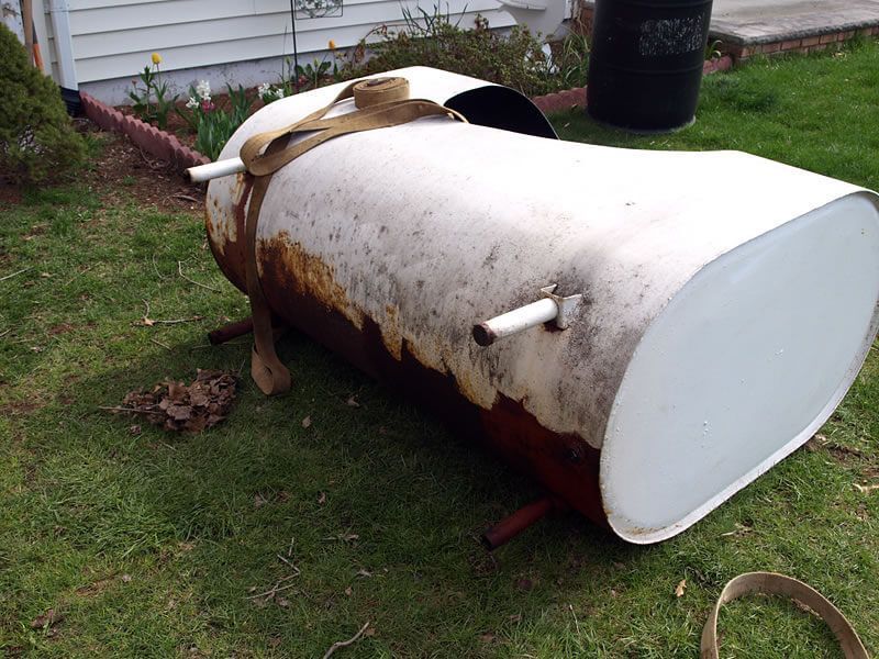 White and rusty metal barrel-shaped outdoor smoker on a green lawn.