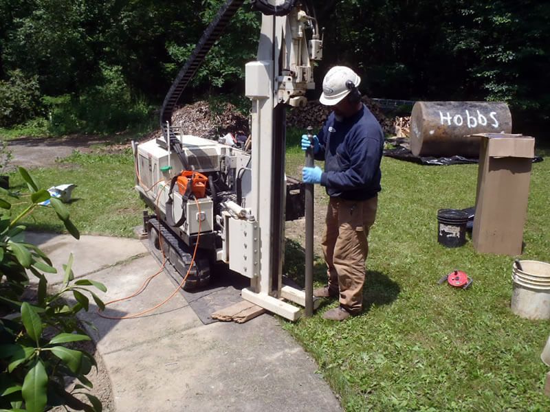 Man operating drilling equipment on grass. A tank labeled 