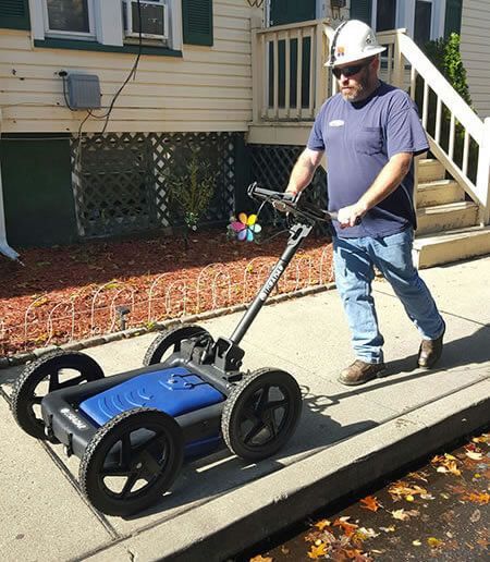 Man in hard hat using ground penetrating radar on a sidewalk.