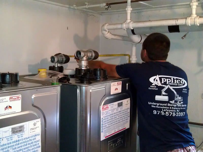 Plumber in blue shirt working on top of a metallic water heater in a utility room.