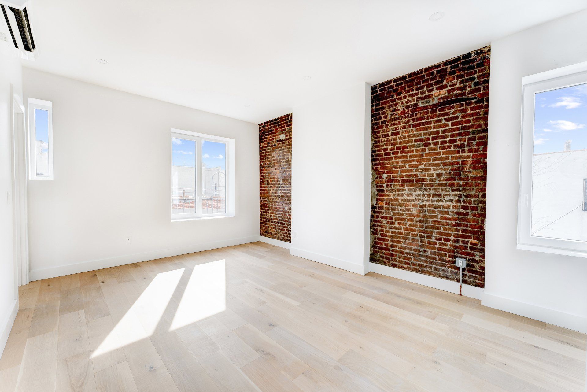 An empty room with hardwood floors and a brick wall.