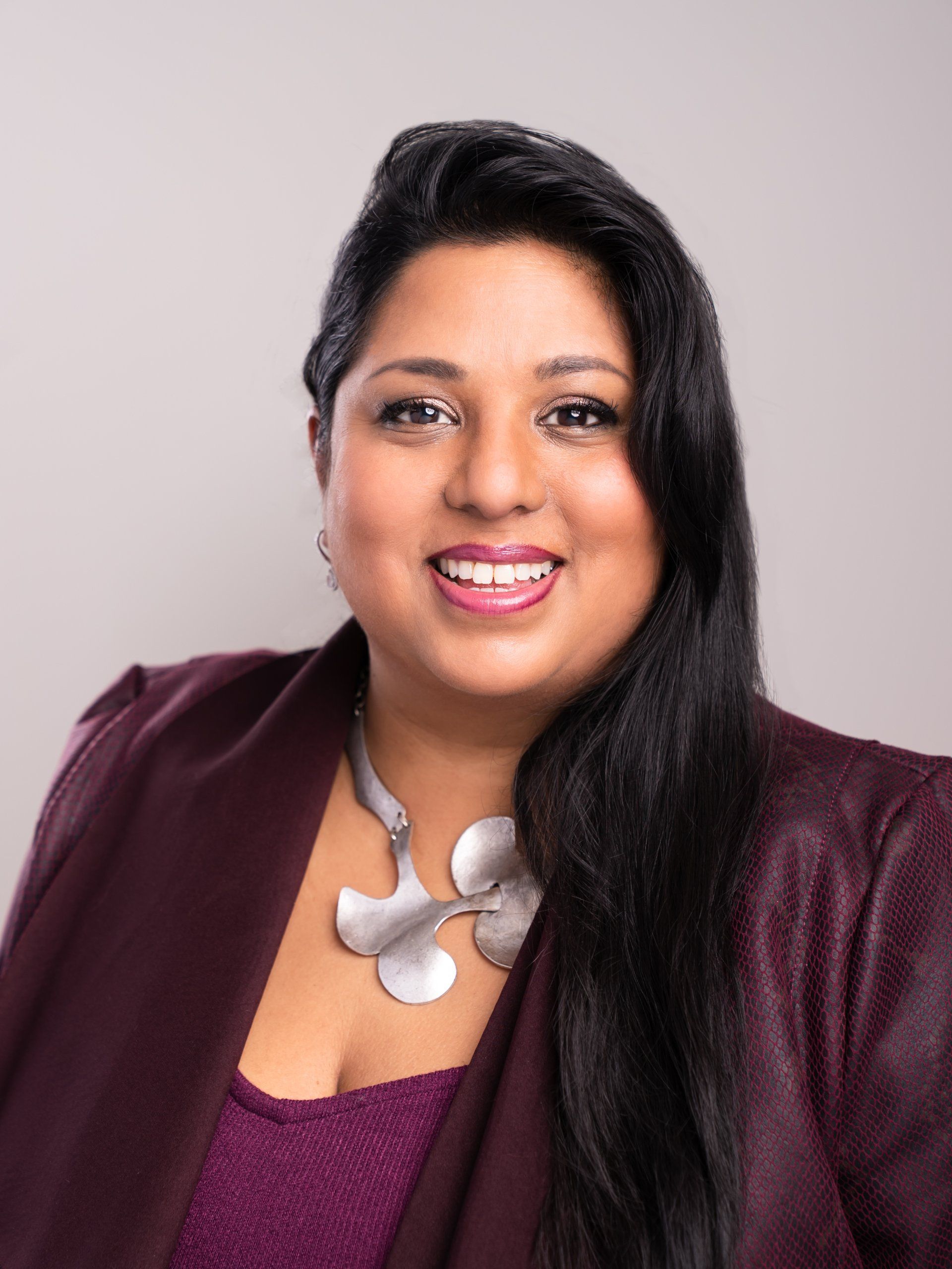 A woman wearing a purple jacket and a silver necklace is smiling for the camera.